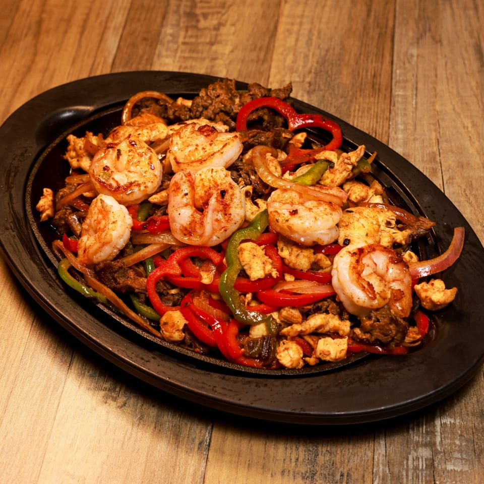 Sizzling Xochitl Cocina & Tequila fajitas with shrimp, chicken, beef, peppers, and onions on a black platter.