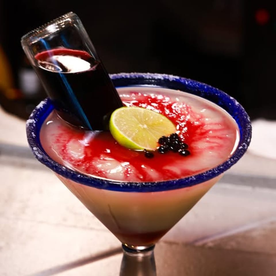 A Xochitl Cocina & Tequila margarita with a small bottle of red liquid, lime, and berries.
