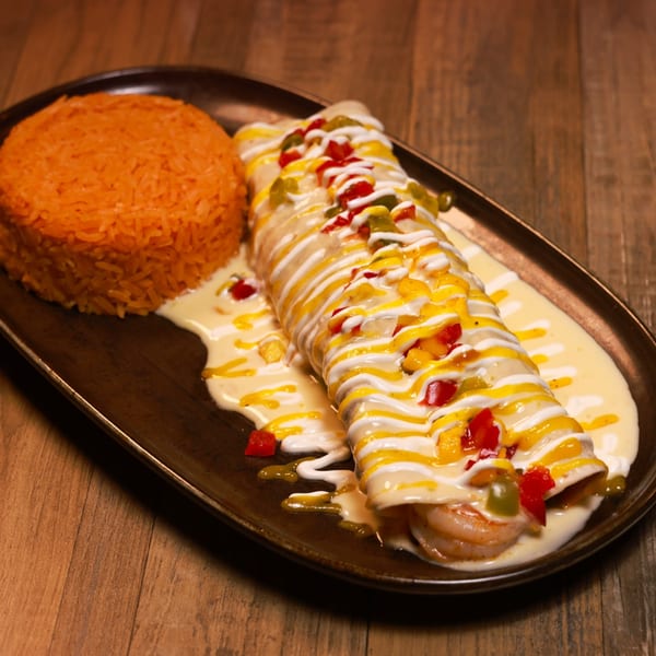 Shrimp enchilada topped with white and yellow sauces, diced peppers, and a side of Mexican rice.