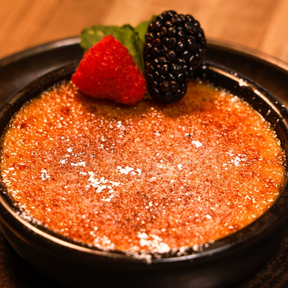 Xochitl Cocina & Tequila's creme brulee dessert, garnished with a raspberry, blackberry, and mint leaf.