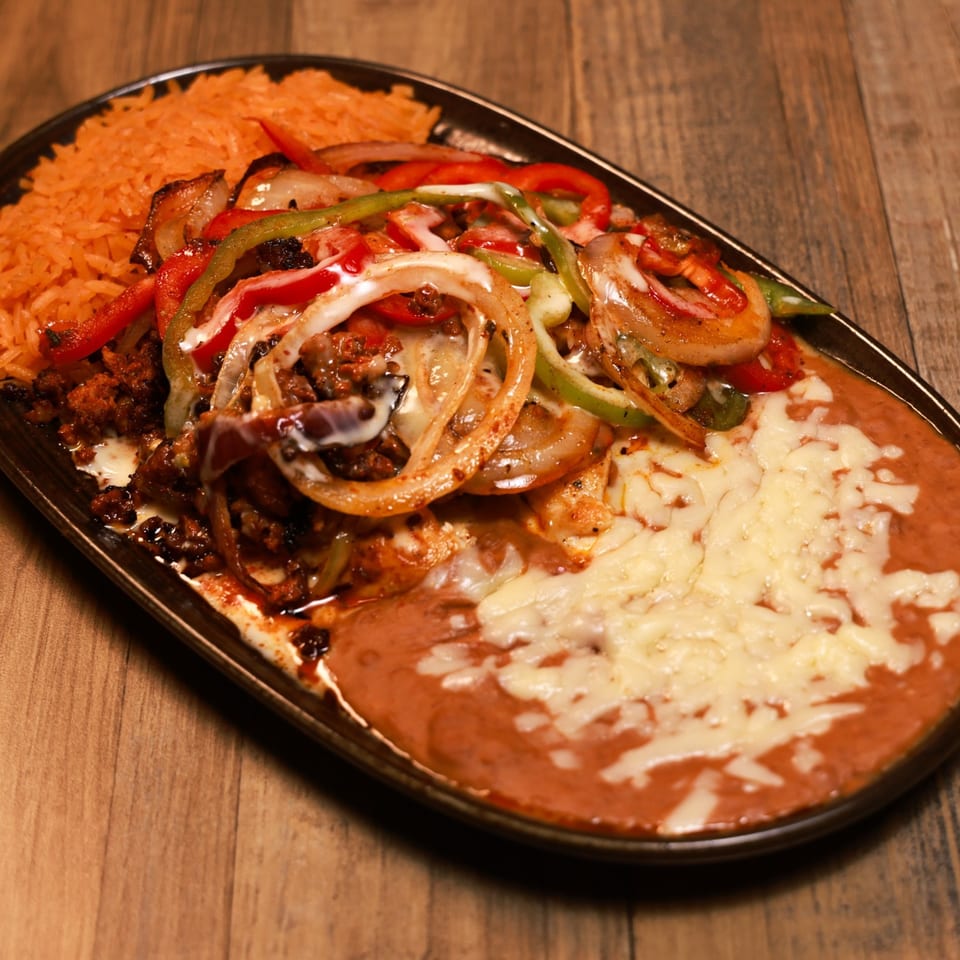 Sizzling Xochitl fajitas with chicken, peppers, onions, rice, and refried beans with melted cheese.
